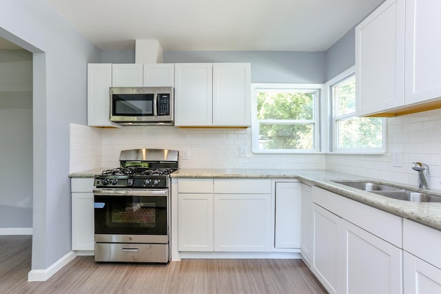 kitchen featuring sink, white cabinets, stainless steel appliances, light stone countertops, and light hardwood / wood-style flooring