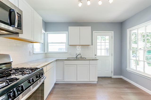 kitchen featuring sink, gas range, white cabinetry, light stone countertops, and decorative backsplash