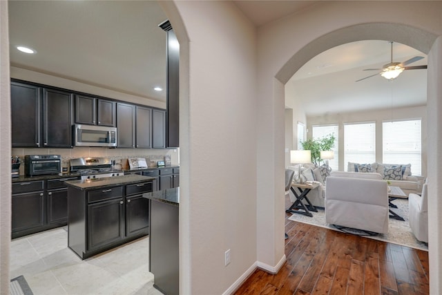 kitchen featuring dark stone countertops, light hardwood / wood-style flooring, backsplash, stainless steel appliances, and ceiling fan