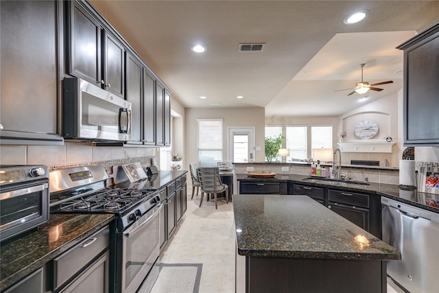 kitchen with sink, dark stone countertops, stainless steel appliances, tasteful backsplash, and a kitchen island