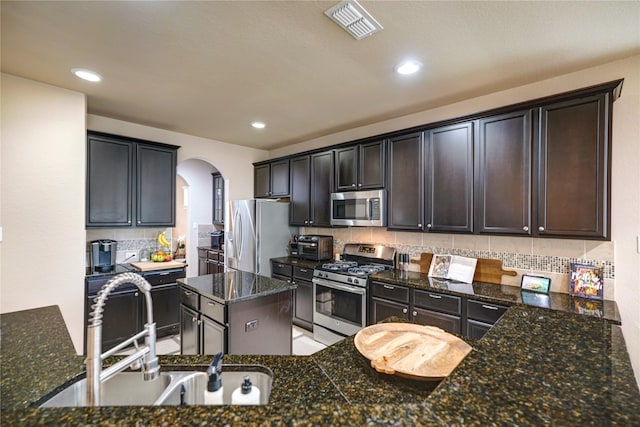 kitchen featuring sink, decorative backsplash, dark stone counters, stainless steel appliances, and dark brown cabinets