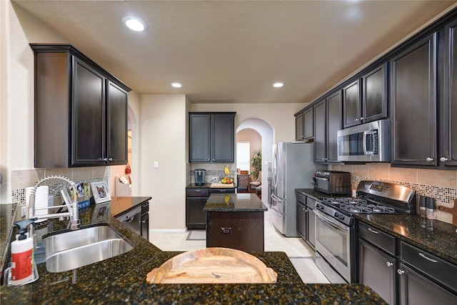 kitchen featuring sink, appliances with stainless steel finishes, dark stone countertops, backsplash, and a kitchen island