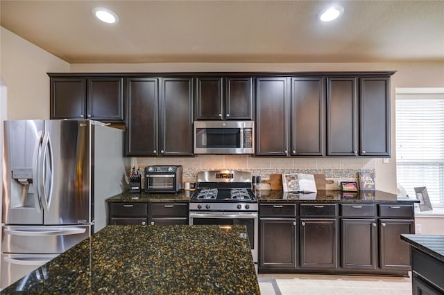 kitchen featuring appliances with stainless steel finishes, dark stone countertops, dark brown cabinetry, and decorative backsplash