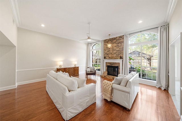 living room featuring crown molding, a fireplace, ceiling fan, and hardwood / wood-style flooring