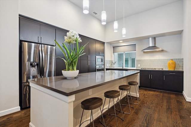 kitchen featuring wall chimney exhaust hood, a breakfast bar area, a kitchen island, stainless steel appliances, and backsplash