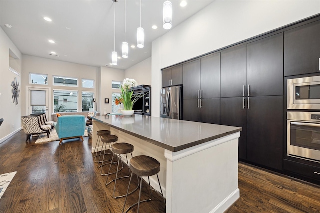 kitchen with dark wood-type flooring, hanging light fixtures, a kitchen breakfast bar, stainless steel appliances, and a center island