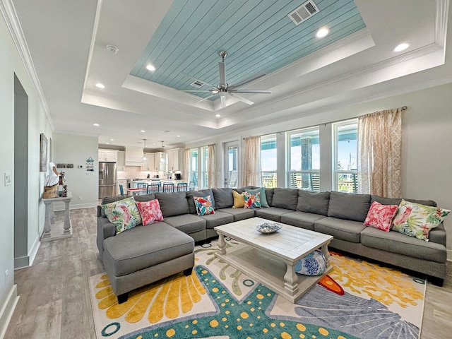 living room with crown molding, ceiling fan, a raised ceiling, and light hardwood / wood-style flooring