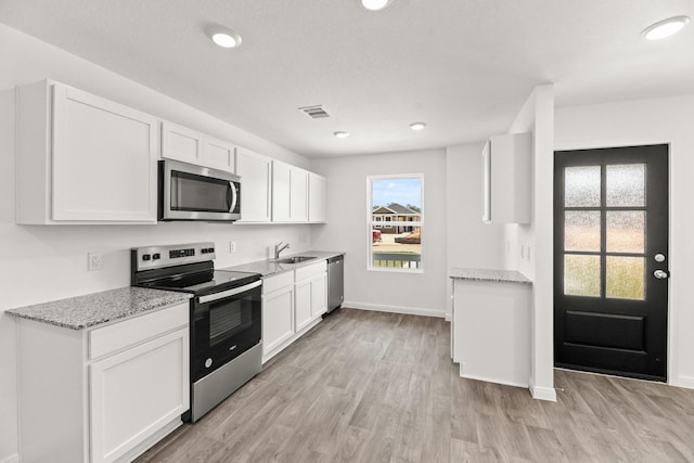 kitchen featuring light stone counters, stainless steel appliances, visible vents, white cabinetry, and light wood finished floors