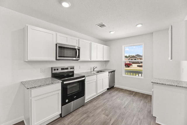 kitchen with visible vents, appliances with stainless steel finishes, white cabinets, light stone countertops, and light wood-type flooring