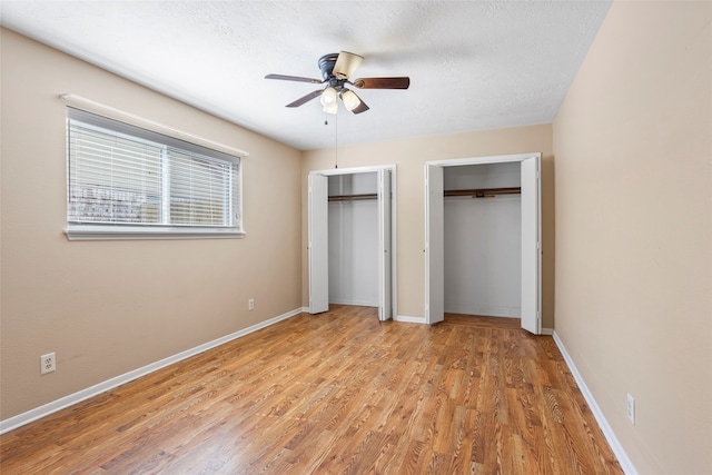 unfurnished bedroom featuring two closets, light hardwood / wood-style floors, ceiling fan, and a textured ceiling