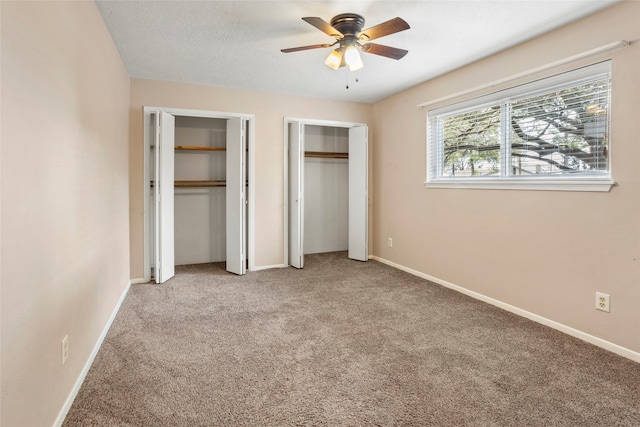 unfurnished bedroom featuring multiple closets, light colored carpet, ceiling fan, and a textured ceiling