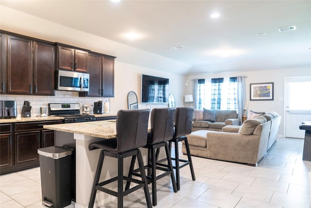 kitchen featuring dark brown cabinetry, a kitchen bar, tasteful backsplash, a center island with sink, and stainless steel appliances