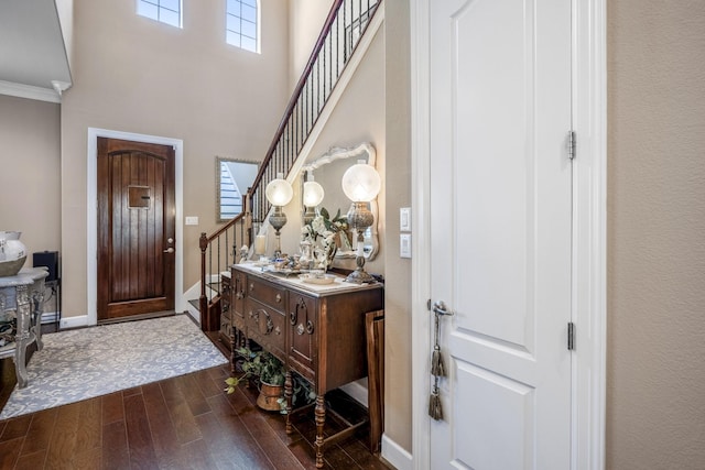 entryway with dark wood-type flooring, ornamental molding, and a high ceiling