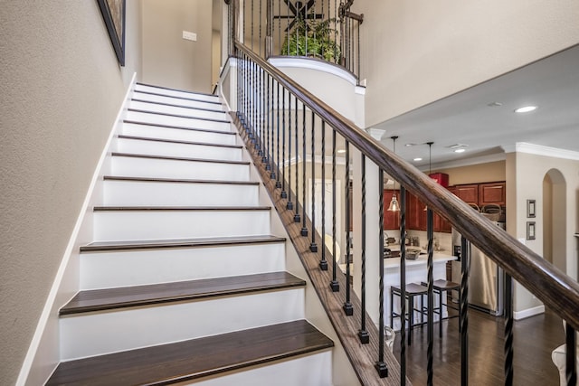 stairway featuring wood-type flooring, ornamental molding, and a towering ceiling