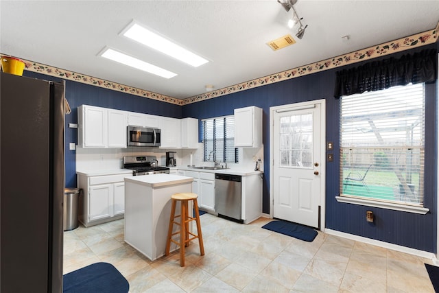 kitchen featuring stainless steel appliances, white cabinetry, a kitchen breakfast bar, a kitchen island, and a healthy amount of sunlight