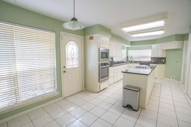 kitchen featuring light tile patterned flooring, white cabinetry, tasteful backsplash, a kitchen island, and stainless steel appliances