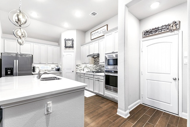 kitchen featuring visible vents, wood finish floors, under cabinet range hood, stainless steel appliances, and a sink