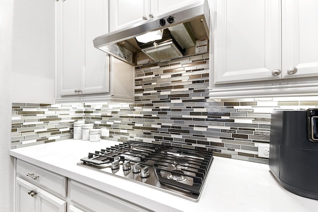 kitchen featuring tasteful backsplash, under cabinet range hood, stainless steel gas cooktop, light countertops, and white cabinets