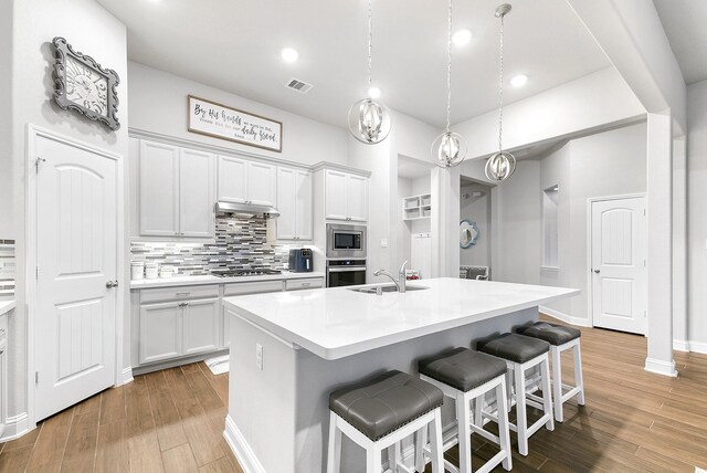 kitchen with sink, white cabinetry, a kitchen island with sink, hanging light fixtures, and stainless steel appliances