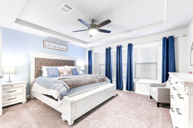 bedroom with visible vents, light carpet, a raised ceiling, a ceiling fan, and baseboards