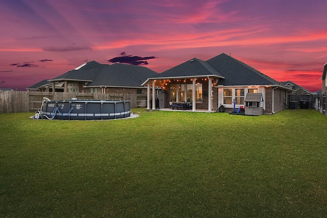 back of property with a lawn, a fenced backyard, a fenced in pool, brick siding, and a patio area