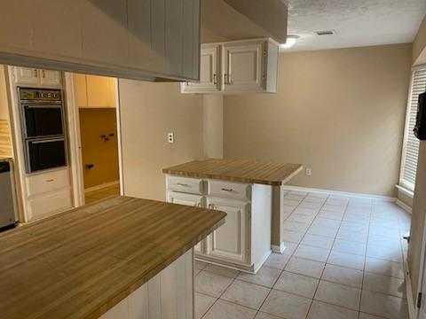 kitchen with light tile patterned floors, a breakfast bar, double wall oven, a textured ceiling, and white cabinets