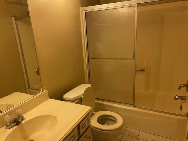 full bathroom with vanity, bath / shower combo with glass door, tile patterned floors, and toilet