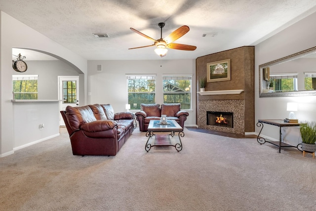 carpeted living room featuring ceiling fan, a large fireplace, and a textured ceiling