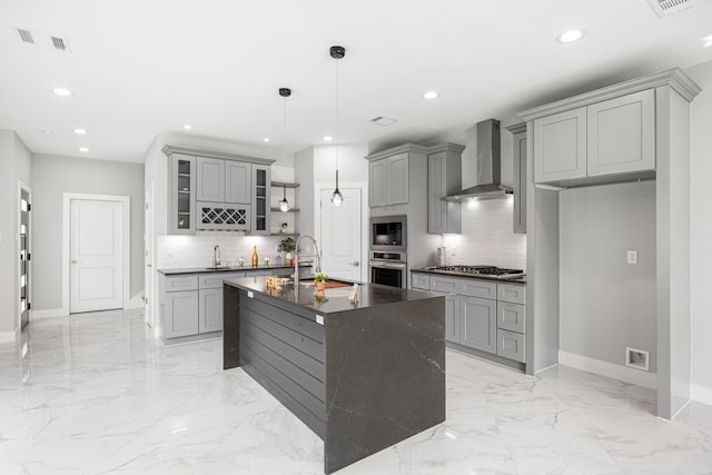 kitchen featuring decorative light fixtures, sink, stainless steel appliances, a center island with sink, and wall chimney exhaust hood