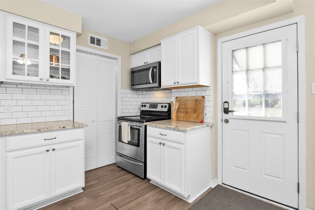 kitchen featuring dark wood-type flooring, appliances with stainless steel finishes, white cabinetry, backsplash, and light stone counters