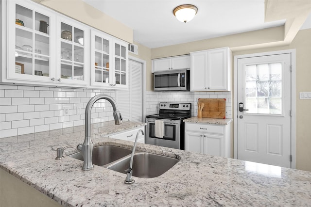 kitchen with stainless steel appliances, light stone countertops, sink, and white cabinets