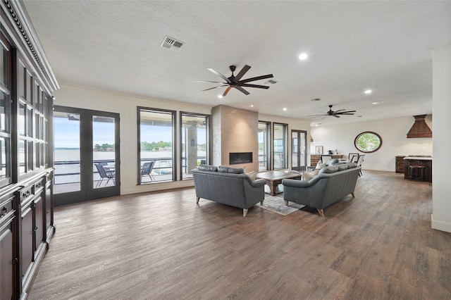 living room featuring a water view, ceiling fan, wood-type flooring, and a textured ceiling