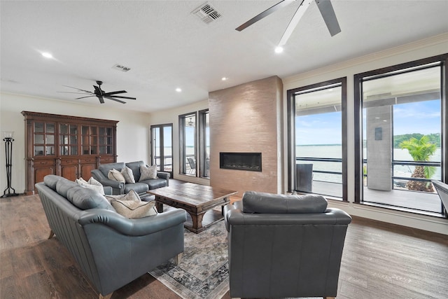 living room featuring crown molding, ceiling fan, hardwood / wood-style floors, a water view, and a large fireplace