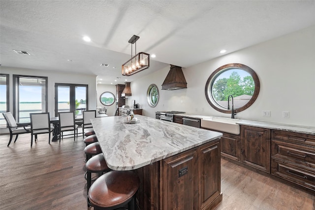 kitchen with a breakfast bar, sink, a center island, hanging light fixtures, and dark hardwood / wood-style floors