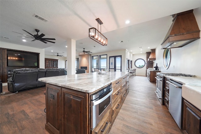 kitchen featuring a kitchen island, decorative light fixtures, custom exhaust hood, light stone counters, and stainless steel appliances