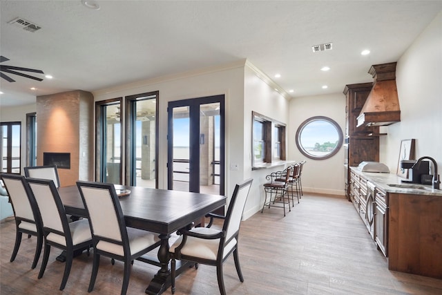 dining room with ornamental molding, a healthy amount of sunlight, sink, and light hardwood / wood-style flooring