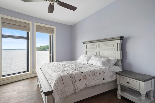 bedroom with hardwood / wood-style floors, ceiling fan, and a water view