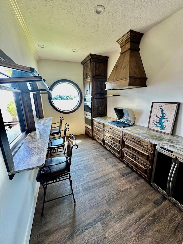 kitchen featuring dark wood-type flooring, light stone counters, dark brown cabinetry, custom range hood, and a textured ceiling