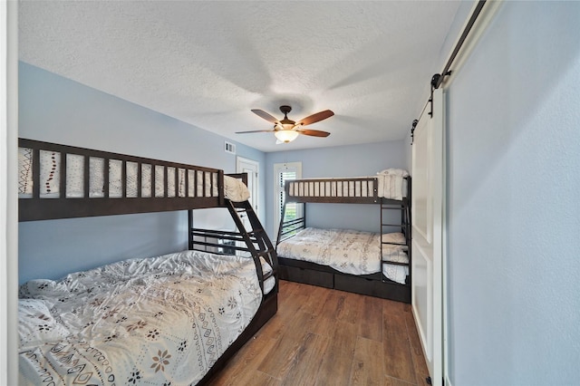 bedroom featuring dark hardwood / wood-style flooring, ceiling fan, a barn door, and a textured ceiling