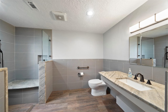 bathroom with hardwood / wood-style floors, a shower, tile walls, vanity, and a textured ceiling