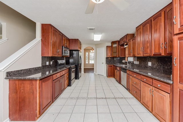 kitchen with sink, light tile patterned floors, appliances with stainless steel finishes, ceiling fan, and dark stone counters