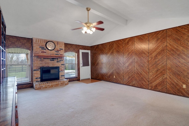 unfurnished living room featuring ceiling fan, a fireplace, carpet floors, lofted ceiling with beams, and wood walls