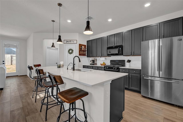 kitchen with pendant lighting, sink, a breakfast bar area, black appliances, and an island with sink