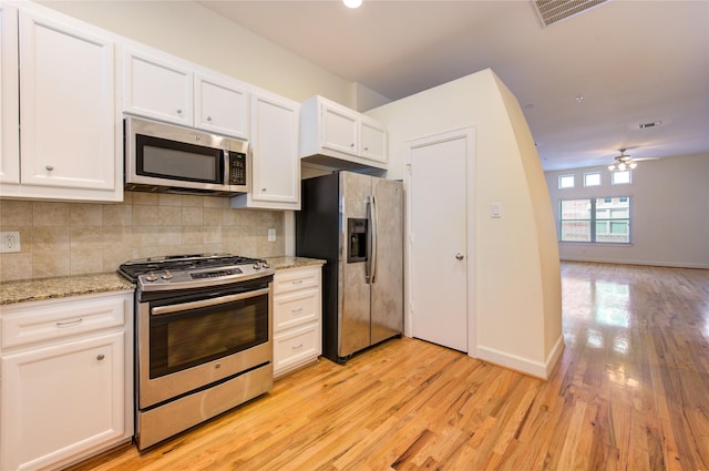 kitchen with light hardwood / wood-style flooring, appliances with stainless steel finishes, white cabinetry, backsplash, and light stone counters