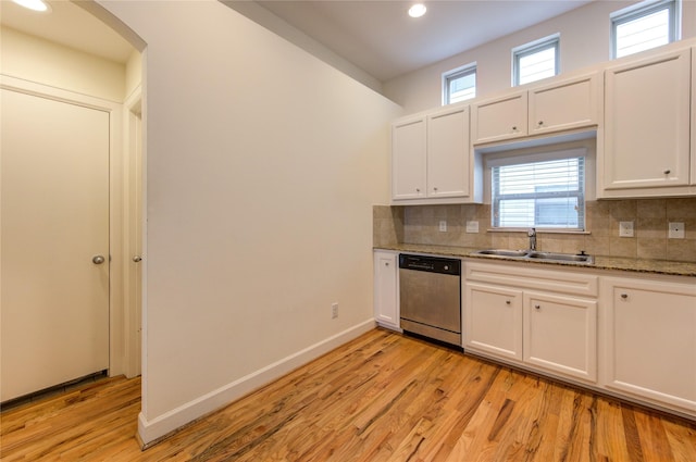 kitchen with tasteful backsplash, sink, white cabinets, stainless steel dishwasher, and light stone countertops