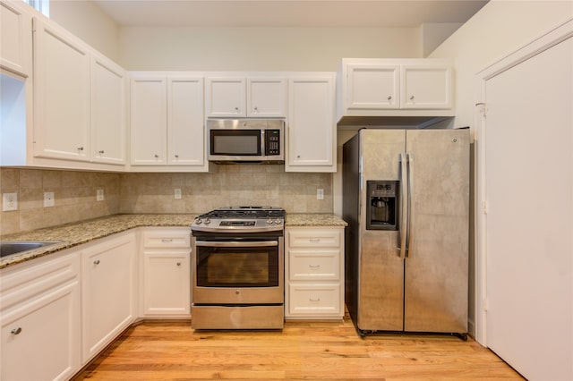 kitchen with light stone countertops, decorative backsplash, stainless steel appliances, and light wood-type flooring