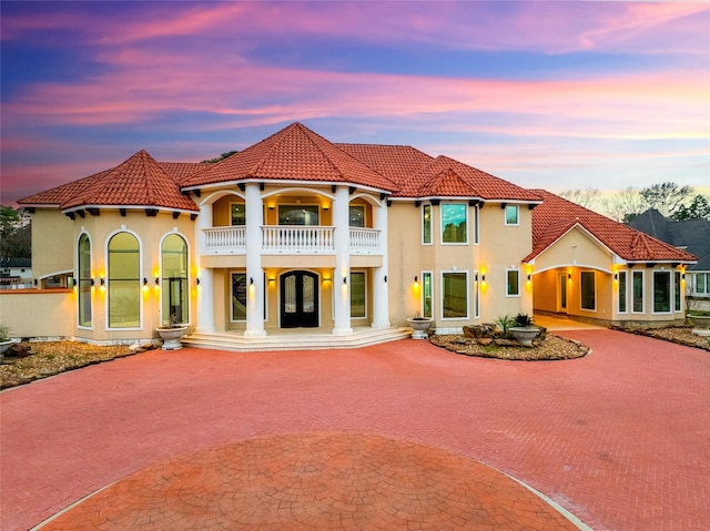 mediterranean / spanish home with a balcony, a tiled roof, decorative driveway, and stucco siding