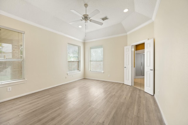 empty room with a raised ceiling, crown molding, ceiling fan, and light hardwood / wood-style flooring