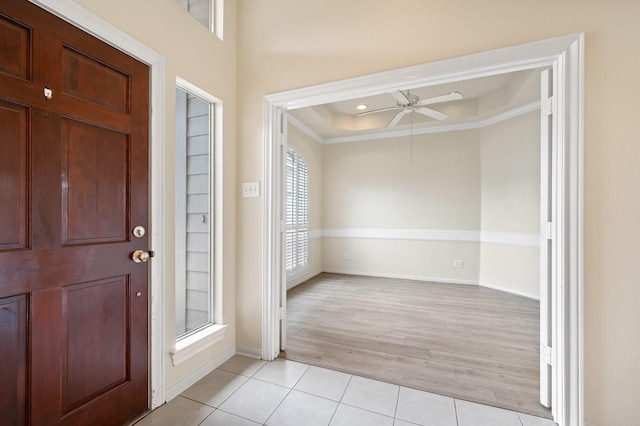 foyer with light tile patterned floors, ornamental molding, a raised ceiling, and ceiling fan