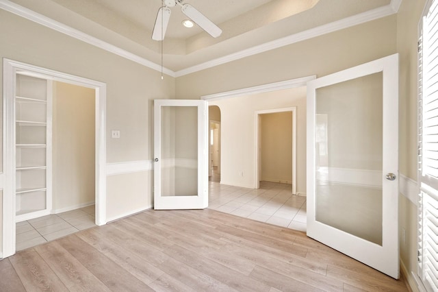 empty room featuring crown molding, ceiling fan, a tray ceiling, and light hardwood / wood-style floors